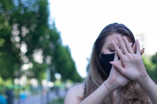 Pretty young blonde woman in medical black face mask. Wearing a t-shirt and jeans shorts. in a park. modern reality. covid-19 concept. copy space. High quality photo