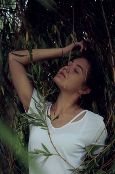 portrait of a flirty beautiful woman in white sport dress holding a tree branch in the tropical forest. Luxury resort.