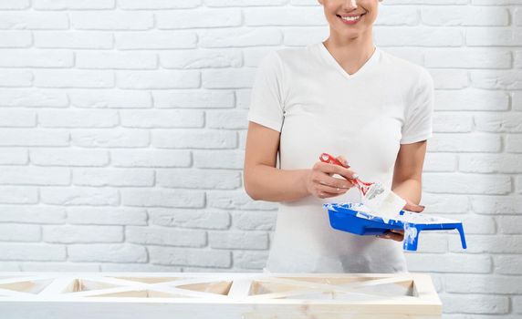 Smiling woman in white shirt holding paint on white background. Concept of preparing for painting wooden rack.