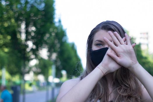 Pretty young blonde woman in medical black face mask. Wearing a t-shirt and jeans shorts. in a park. modern reality. covid-19 concept. copy space. High quality photo