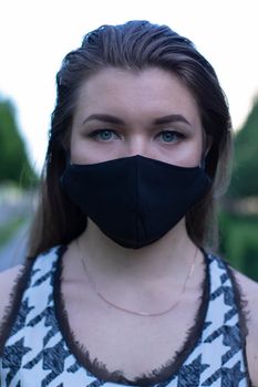 Pretty young blonde woman in medical black face mask. Wearing a t-shirt and jeans shorts. in a park. modern reality. covid-19 concept. copy space. High quality photo