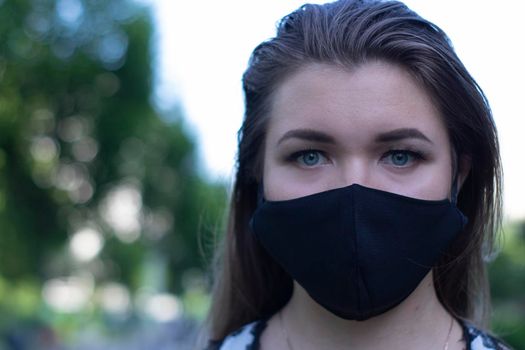 Pretty young blonde woman in medical black face mask. Wearing a t-shirt and jeans shorts. in a park. modern reality. covid-19 concept. copy space. High quality photo