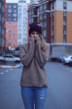 urban portrait of a pensive beautiful woman in knitted brown sweater, jeans and black hat. in the parking lot.