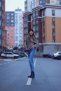 urban portrait of a happy flirty beautiful woman in knitted brown sweater, jeans and black hat. in the parking lot.