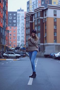 urban portrait of a happy flirty beautiful woman in knitted brown sweater, jeans and black hat. in the parking lot.