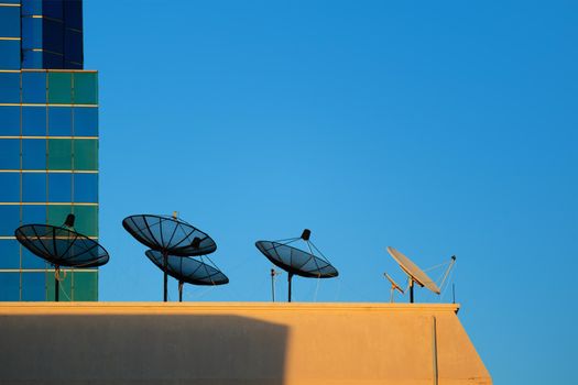 Satellite dish on top of a tall building with a background sky