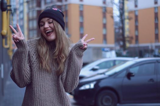 urban portrait of a happy flirty beautiful woman in knitted brown sweater, jeans and black hat. in the parking lot.