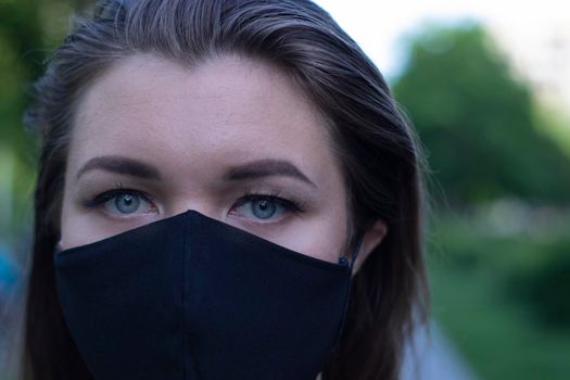 Pretty young blonde woman in medical black face mask. Wearing a t-shirt and jeans shorts. in a park. modern reality. covid-19 concept. copy space. High quality photo