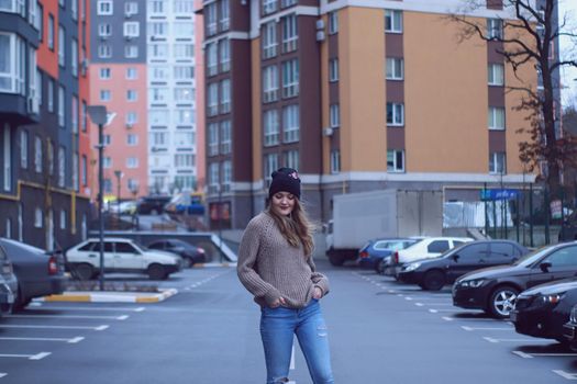 urban portrait of a happy flirty beautiful woman in knitted brown sweater, jeans and black hat. in the parking lot.