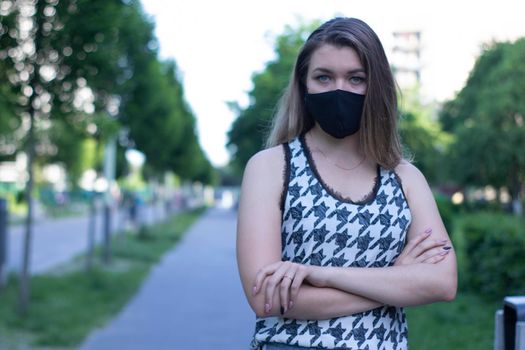 Pretty young blonde woman in medical black face mask. Wearing a t-shirt and jeans shorts. in a park. modern reality. covid-19 concept. copy space. High quality photo