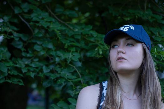 Pretty young blonde woman wearing a t-shirt, jeans shorts and cap. in a park. copy space. High quality photo