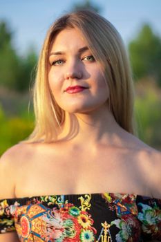 overlight bright portrait of a charming attractive blonde in flowery dress in the field.