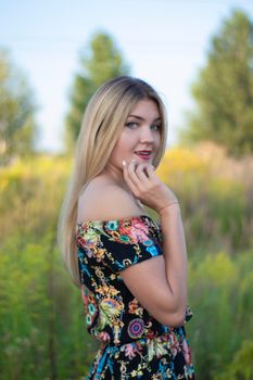 overlight bright portrait of a charming attractive blonde in flowery dress in the field.