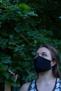 Pretty young blonde woman in medical black face mask. in a bush, forest. covid-19 concept. modern reality. copy space. High quality photo