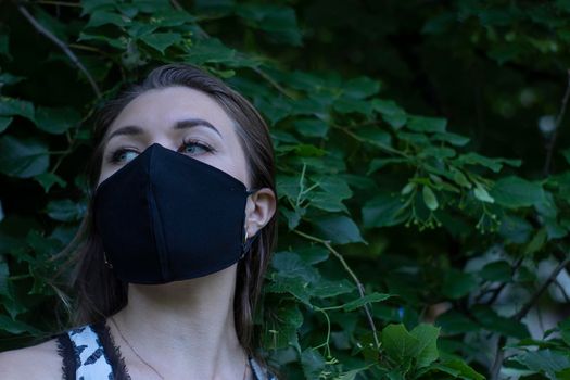 Pretty young blonde woman in medical black face mask. in a bush, forest. covid-19 concept. modern reality. copy space. High quality photo