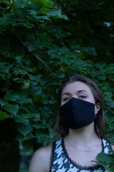 Pretty young blonde woman in medical black face mask. in a bush, forest. covid-19 concept. modern reality. copy space. High quality photo