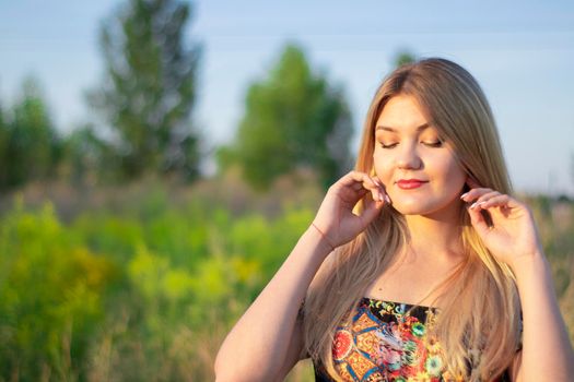 overlight bright portrait of a charming attractive blonde in flowery dress in the field.