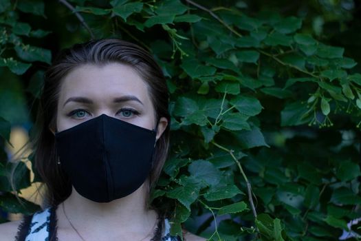Pretty young blonde woman in medical black face mask. in a bush, forest. covid-19 concept. modern reality. copy space. High quality photo
