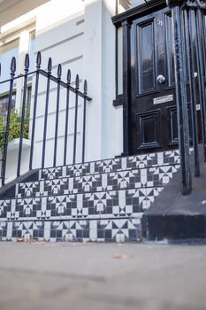 Low angle view of Black and white tiles on the stairs of white British house with black door. Beautiful tiles on stairs of English house with victorian architecture. Colorful London neighborhood