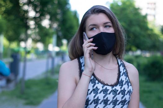 Pretty young blonde woman in medical black face mask. Wearing a t-shirt and jeans shorts. in a park. covid-19 concept. copy space.