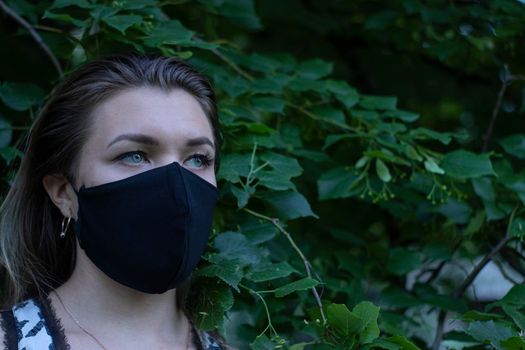 Pretty young blonde woman in medical black face mask. in a bush, forest. covid-19 concept. modern reality. copy space. High quality photo