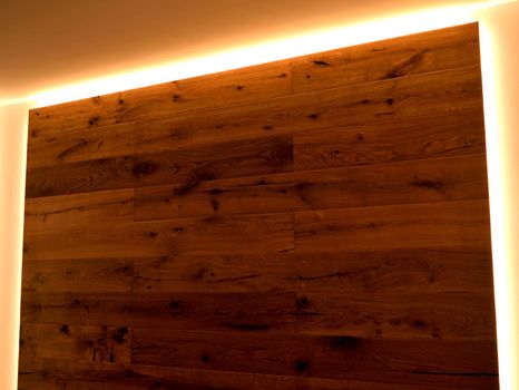 A closeup of a wall covered with parquet with its natural veins, delimited by LED strips.