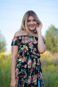 overlight bright portrait of a charming attractive blonde in flowery dress in the field.