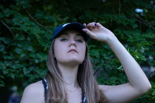 Pretty young blonde woman wearing a t-shirt, jeans shorts and cap. in a park. copy space. High quality photo