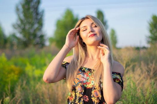 overlight bright portrait of a charming attractive blonde in flowery dress in the field.