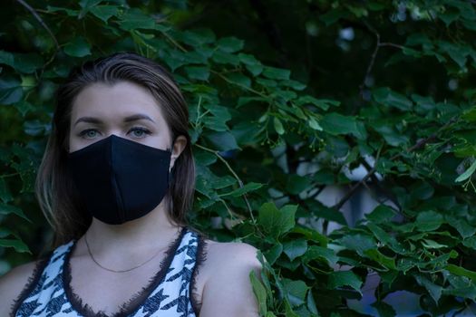 Pretty young blonde woman in medical black face mask. in a bush, forest. covid-19 concept. modern reality. copy space. High quality photo