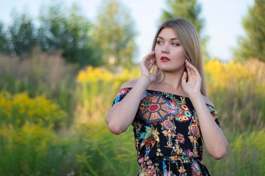 overlight bright portrait of a charming attractive blonde in flowery dress in the field.