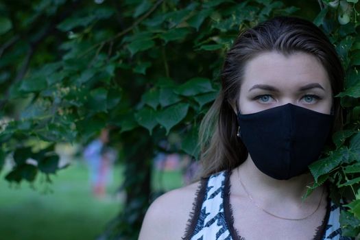 Pretty young blonde woman in medical black face mask. in a bush, forest. covid-19 concept. modern reality. copy space. High quality photo