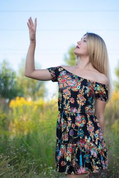 overlight bright portrait of a charming attractive blonde in flowery dress in the field.