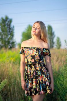 overlight bright portrait of a charming attractive blonde in flowery dress in the field.