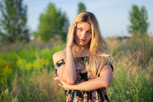 overlight bright portrait of a charming attractive blonde in flowery dress in the field.