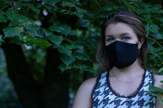 Pretty young blonde woman in medical black face mask. in a bush, forest. covid-19 concept. modern reality. copy space. High quality photo