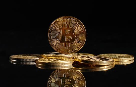 Leader in cryptocurrency Bitcoin BTC on a top of coins against black mirror surface. Closeup golden coin with bitcoin logo. А heap of decentralized digital currency. Crypto payment. Electronic money.