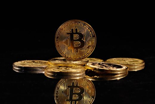 Leader in cryptocurrency Bitcoin BTC on a top of coins against black mirror surface. Closeup golden coin with bitcoin logo. А heap of decentralized digital currency. Crypto payment. Electronic money.