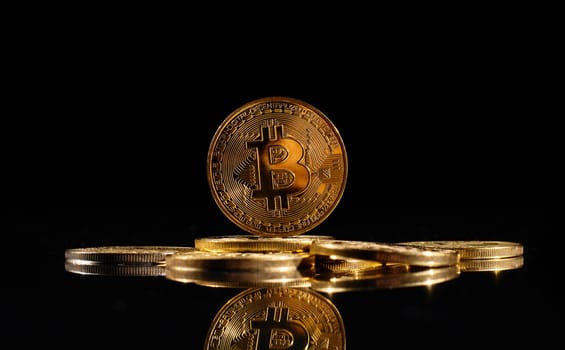 Leader in cryptocurrency Bitcoin BTC on a top of coins against black mirror surface. Closeup golden coin with bitcoin logo. А heap of decentralized digital currency. Crypto payment. Electronic money.