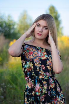 overlight bright portrait of a charming attractive blonde in flowery dress in the field.