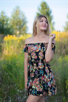 overlight bright portrait of a charming attractive blonde in flowery dress in the field.