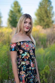 overlight bright portrait of a charming attractive blonde in flowery dress in the field.