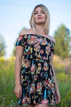 overlight bright portrait of a charming attractive blonde in flowery dress in the field.