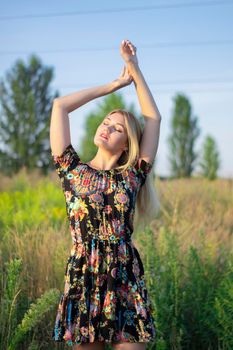 overlight bright portrait of a charming attractive blonde in flowery dress in the field.