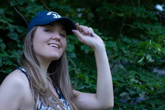 Pretty young blonde woman wearing a t-shirt, jeans shorts and cap. in a park. copy space. High quality photo