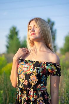 overlight bright portrait of a charming attractive blonde in flowery dress in the field.