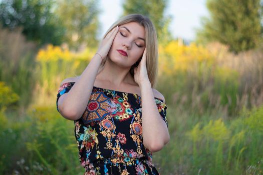 overlight bright portrait of a charming attractive blonde in flowery dress in the field.