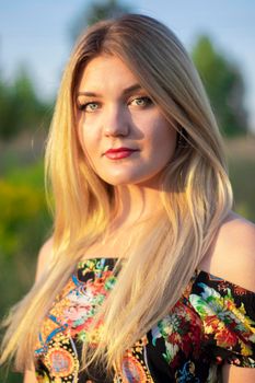 overlight bright portrait of a charming attractive blonde in flowery dress in the field.