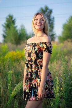 overlight bright portrait of a charming attractive blonde in flowery dress in the field.