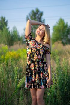 overlight bright portrait of a charming attractive blonde in flowery dress in the field.